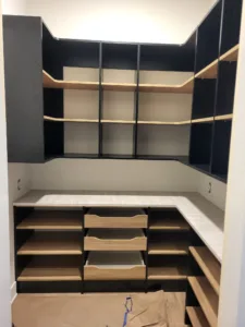 Built-in closet cabinetry with black frame, open shelving, and center drawers, unfinished raw wood
