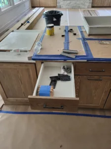 Kitchen cabinet drawer open showing contents, countertop taped off during installation