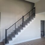 Completed stair railing with horizontal metal rods, black newel posts, and painted treads and risers.