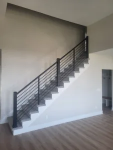 Finished interior staircase with horizontal metal rod railing and carpeted treads