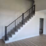 Completed stair railing with horizontal black metal rods between newel posts, gray treads, and white risers.