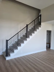 Finished staircase with horizontal black metal rod railing between newel posts, gray treads