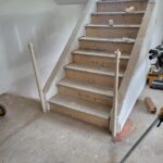 This photo shows the installation of a handrail on a staircase, with unfinished steps and temporary supports visible. The work is currently in progress.