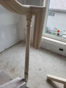 Painted white turned wood newel post at the foot of a curved staircase near a large window