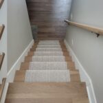 Staircase with carpet treads, wood nosing, painted baseboard, and wall-mounted handrail with brackets.
