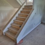 Finished wood risers and treads installed on staircase with painted walls and wood handrail, pre-paint stage.