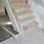 Staircase framing in progress with raw wood risers, composite treads, and drywall walls—pre-finish carpentry stage.