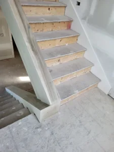 Interior staircase framing stage with raw plywood treads and exposed wall studs