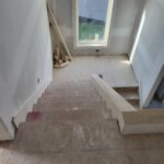 Staircase with finished treads and risers installed, drywall walls, and exterior door opening at landing.