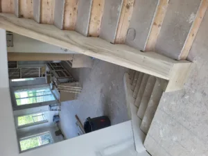 Raw wood beam spanning a stairwell opening with exposed roof framing above, unfinished