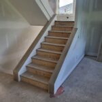 Stair assembly with finished wood treads, risers, skirt boards, and handrail—raw wood ready for paint.