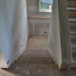 Staircase framing in progress with drywall walls and raw wood stairs during construction phase.