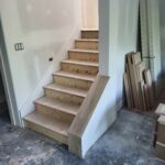 Finished wood skirt board installed on staircase with raw wood treads and primed drywall walls.