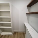 Completed closet with white painted built-in shelving unit and dark wood floating shelves, ready for use.
