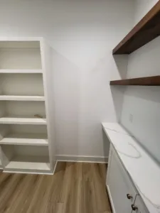 Finished closet with painted white built in shelving and a dark wood floating shelf on the wall