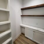 Finished closet with white painted shelving, dark wood floating shelves, base cabinet with countertop, and hardwood floor.