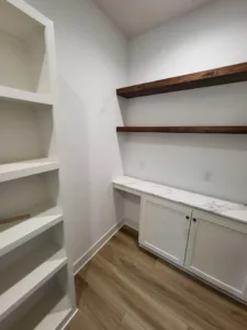 Finished closet with painted white shelving, dark wood floating shelf, and a white counter, hardwood floor