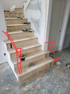 Interior stair under construction, wood treads, white-painted skirt board, layout marks visible.