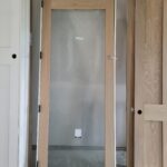 Hollow-core interior door slab with full-lite glass panel, uninstalled and leaning in staging area.