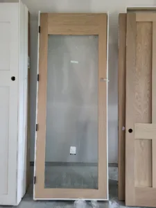 Wood door slab with a full lite glass panel leaning among other slabs in a staging area