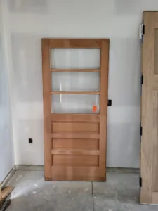 Unfinished wood door slab with glass lites over a paneled base, leaning indoors before installation