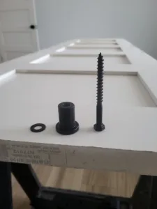 Screw, sleeve cap, and washer staged on a paneled door before pull hardware installation