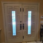 Finished painted exterior double doors with glass sidelites, decorative hardware, and installed casing trim.