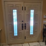 Finished exterior double doors with sidelights, painted cream, decorative panels, black hardware installed.