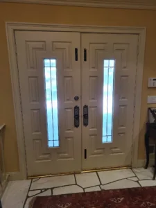 Painted cream double entry doors with narrow glass insert, decorative molding and black hardware, completed