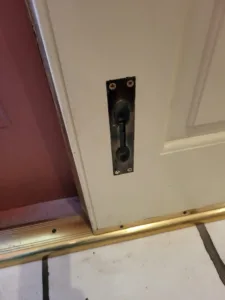 Black finish pocket door edge pull installed near the floor, brass door track visible below
