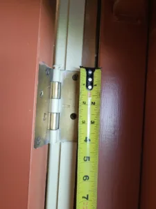 Butt hinge mortised into a painted door jamb with a tape measure held alongside it