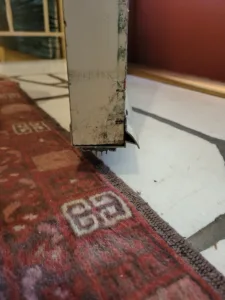 Door jamb extension at floor level where the frame meets a patterned rug and tile