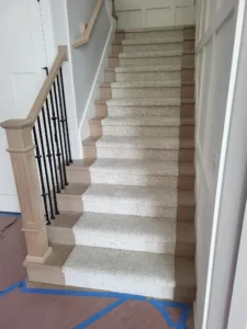 Completed staircase with a carpet runner, black iron balusters, and an unfinished wood handrail