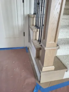Stepped wood cap trim atop a stair knee wall beside a newel post with iron balusters