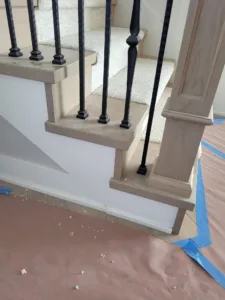 Wood stair tread end caps with a wrapped return, black iron balusters set in, paper protected floor