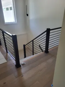 Finished staircase landing with horizontal black metal rod railing and black square posts