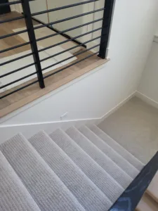 Black horizontal-rod railing on a wood capped half wall overlooking carpeted stairs.