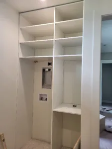 White closet shelving with cubby storage and a wall cutout with electrical outlet, finished