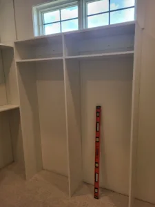 Primed face frame closet shelving with vertical dividers below two windows, ready for paint.