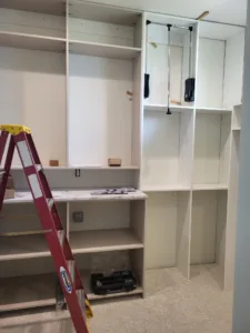 Closet shelving installation in progress with vertical dividers, hanging rod hardware, and ladder