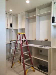 White painted closet shelving with open cubby storage, center hanging rod, and lower workspace
