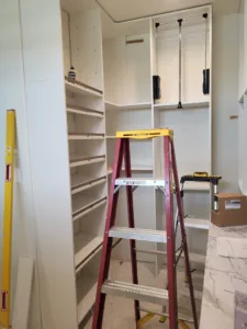 Closet shelving column in progress with multiple tiers, pull down rod hardware, and ladder present