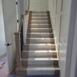 Completed staircase with wood treads, stair runner, iron balusters, newel post, and painted casing and doors.