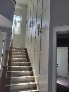 Painted geometric wall paneling installed along a staircase, with wall sconces and carpeted stair treads