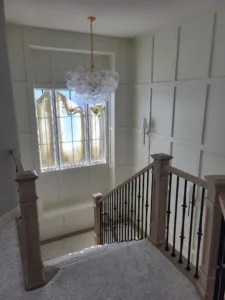 Finished stairwell landing with painted wainscoting, wood newel post, and iron balusters below