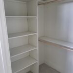 Completed walk-in closet with painted shelving units and hanging rod installed on both walls.