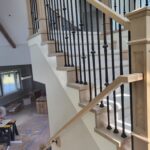 Iron balusters installed between wood handrails and treads with black finish caps and newel posts.