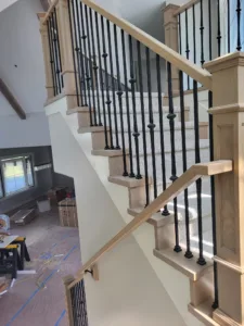 Staircase with raw wood handrail and treads, black iron balusters, and a carpet runner, still unfinished