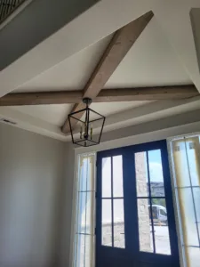 Dark stained wood beam crossing a vaulted entry ceiling above a lantern pendant and glass door