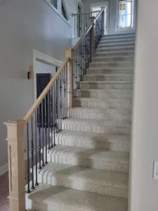 Long view up carpeted staircase with vertical black iron balusters and wood cap rail